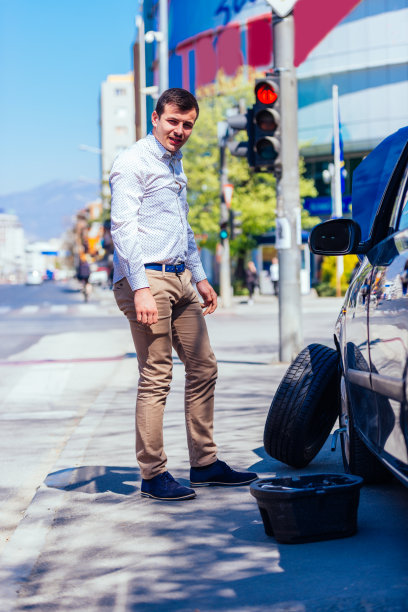 在一个阳光明媚的日子里，一位满身是汗、疲惫不堪的年轻企业家在换车胎时擦着额头上的汗水图片下载