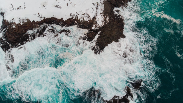 这张照片是由无人机从空中拍摄的，我们可以从鸟瞰的角度看到，白雪覆盖的石头海岸上有一片泡沫图片下载