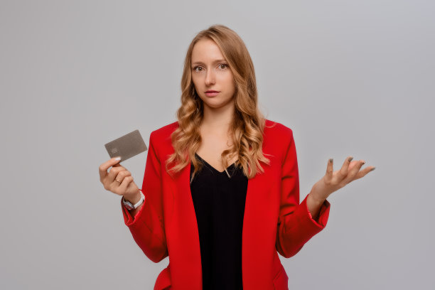 一幅困惑的年轻女企业家的肖像，拿着手机和信用卡，茫然地耸耸肩膀，不认识史密斯，站在白色的背景上图片下载