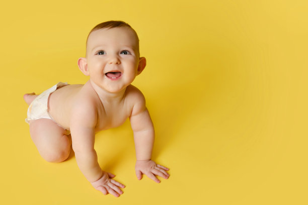 快乐的学步婴儿在工作室黄色的背景下大笑。有趣的孩子男孩在六个月的年龄爬行和微笑，复制空间图片下载