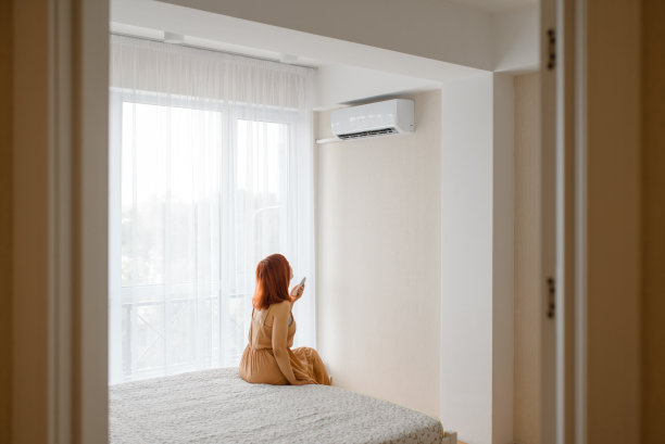 年轻美丽的女子在她白色的公寓里打开空调，享受凉爽。图片下载