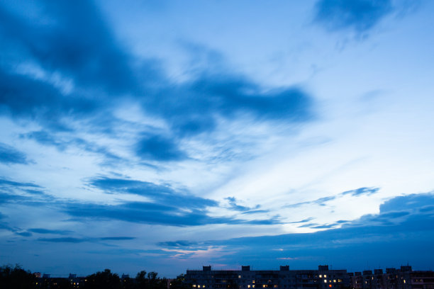 在深蓝色的天空中，只能看到房屋的轮廓。日落的天空在房子的屋顶上与郊区的小房子在一条水平线上。图片下载