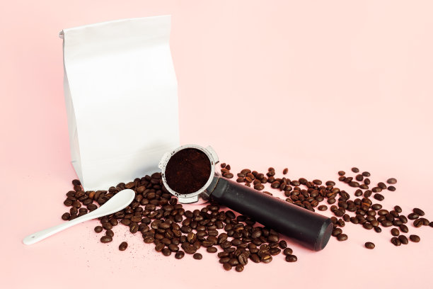 白箔咖啡豆袋模拟与白色勺子和portfilter在淡粉色背景的咖啡豆图片下载