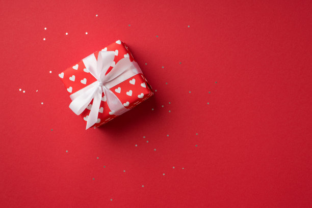 俯视图照片的情人节装饰发光亮片礼品盒在红色包装纸与心脏图案和白色丝带蝴蝶结孤立的红色背景与空白空间图片下载
