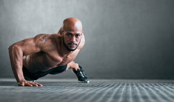 一个英俊的年轻男性运动员在灰色背景下做单手俯卧撑的全身肖像图片下载
