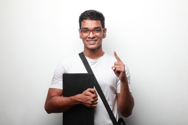 一名年轻的印度裔男子面带微笑，手里拿着一台笔记本电脑，竖起了他的手指图片下载