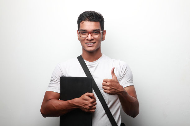 一名印度裔年轻人微笑着拿着笔记本电脑，竖起大拇指图片下载