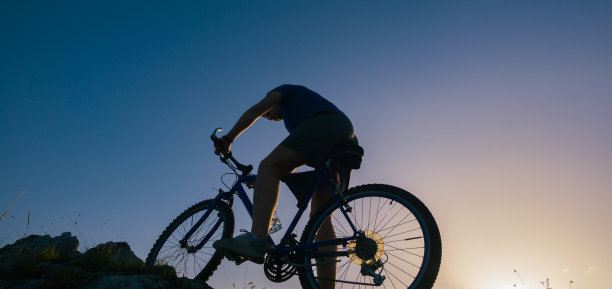 一个健康的男性山地自行车骑他的剪影在岩石粗糙的地形上的日落上山。图片下载