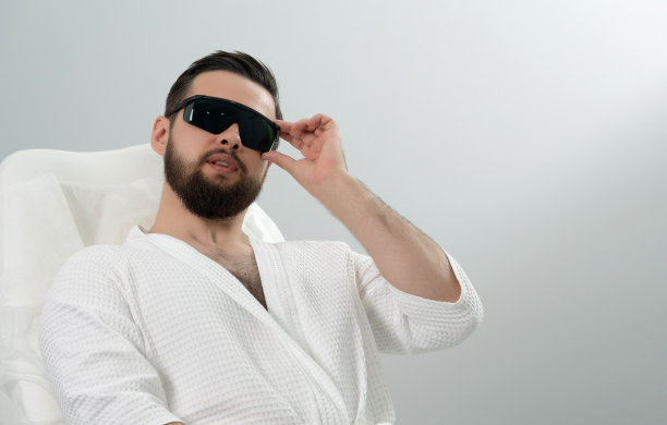 在美容诊所，一名大胡子男子在接受专业美容师的激光面部治疗前坐着。健康男性生活方式理念图片下载