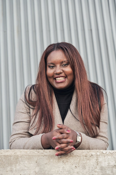 年轻的非洲裔美国女性的肖像，穿着西装，留着长发，手放在墙上看着相机。图片下载