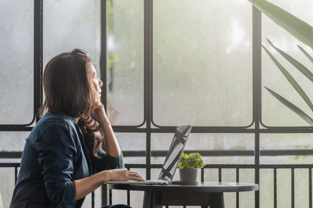 体贴的亚洲妇女在笔记本电脑上工作，看向别处思考解决问题在家庭办公室，认真的妇女在早上寻找灵感。图片下载