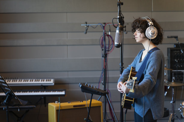 一个年轻的女歌手在一间乱糟糟的录音室里用她的吉他录制歌曲图片下载
