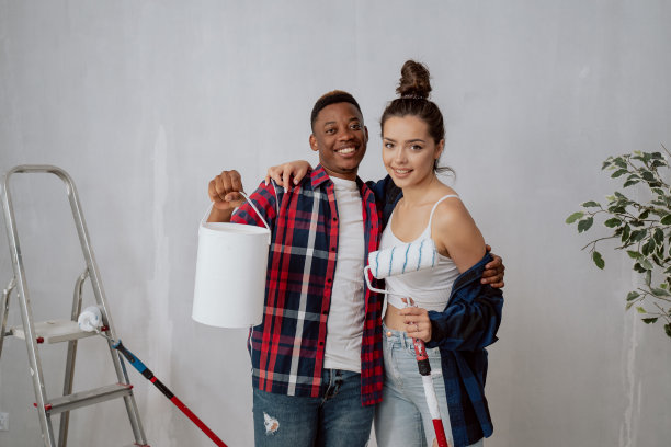 英俊的黑皮肤男孩拿着油漆罐，拥抱着手里拿着墙辊的漂亮女人，夫妇拥抱，他们一起装修新公寓，绘画，整理图片下载
