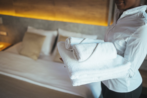 年轻的酒店服务员正在用干净的毛巾铺床。图片下载