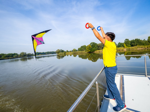 年轻人正站在漂浮的房子的阳台上，试图在天空中放飞明亮的风筝，侧视图照片图片下载