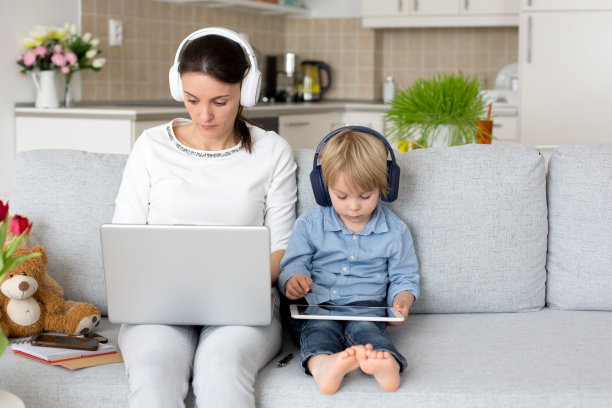 母亲，在她的笔记本电脑上工作和打电话，孩子在她旁边玩耍在家里图片下载