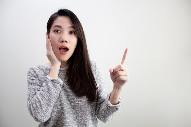 亚洲美女是触摸脸颊和张开的嘴，用另一只手微笑和幸福地指出或指向广告推广和信息的空间。图片下载