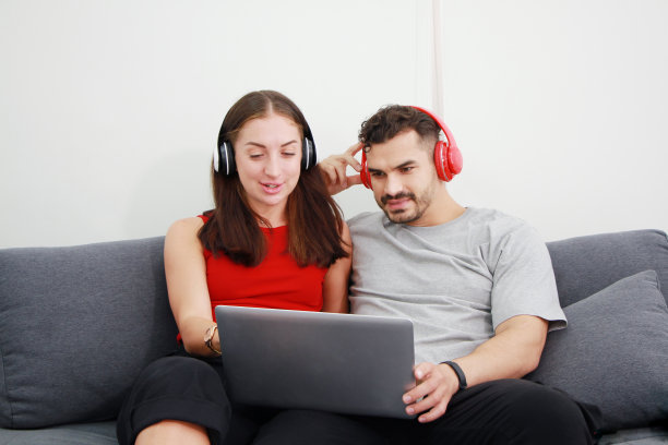 年轻的白种人情侣们喜欢在客厅里用耳机和笔记本电脑一起听在线音乐。婚姻生活方式与度假关系的概念。图片下载