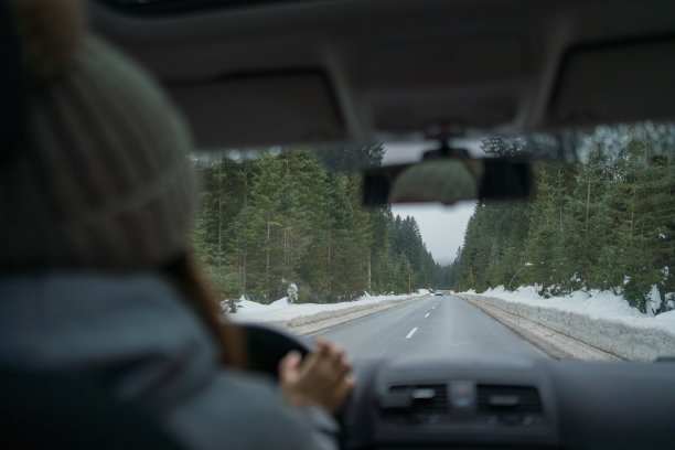 一名年轻女子开着车在雪原中穿过森林图片下载