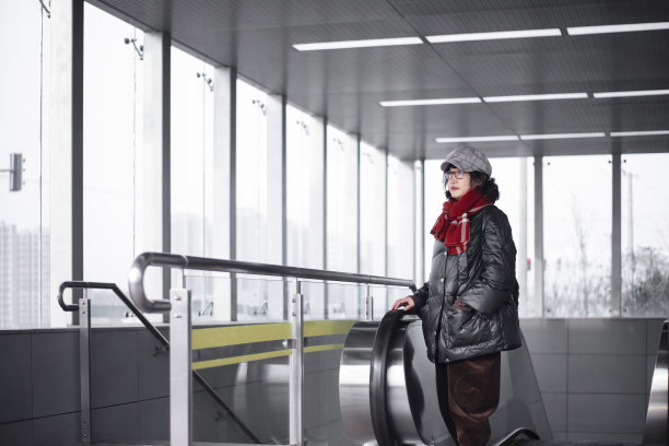 图为，一位东亚女性乘客站在自动扶梯的入口处，向左边眺望现代城市的通勤者。图片下载