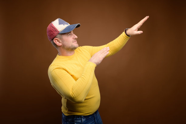 白人胖乎乎的跳舞男子，穿着休闲的牛仔裤、夹克和帽子。他的手指向一边跳舞图片下载