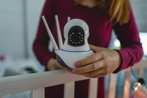 一名不知名的女性母亲在家里卧室的婴儿床上调整和安装监控摄像头，晚上在黑暗的房间里睡觉时，看着摇篮里的孩子图片下载