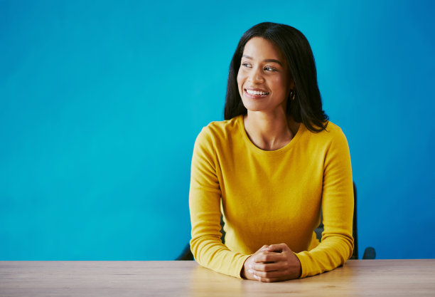 剪裁照片的一个有吸引力的年轻女子看起来深思熟虑，而坐在她的办公桌在工作室的蓝色背景图片下载