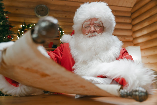 圣诞老人坐在书房的书桌前，展开写着孩子们名字的卷轴，我们从低角度看到了他图片下载