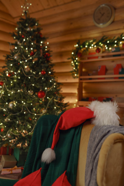 圣诞室内，圣诞老人的房子里有一个舒适的木制房间，装饰的圣诞树和扶手椅上有圣诞老人的帽子图片下载