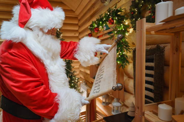 圣诞老人站在一个装饰着节日木墙的房子里，展开写有孩子们名字的卷轴图片下载