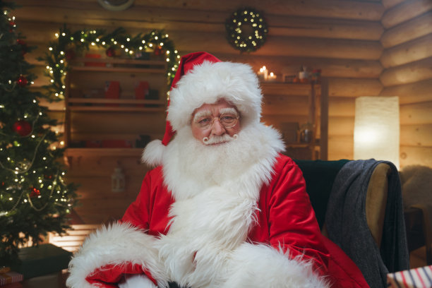 像样的圣诞老人坐在办公室的扶手椅上，带着花环和圣诞树，看着镜头图片下载