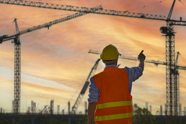 在工业建筑房地产项目现场工作的亚洲工程师或投资者和工人。专业团队对商业、大型建筑项目进行检查。背景起重机摩天大楼。“n图片下载