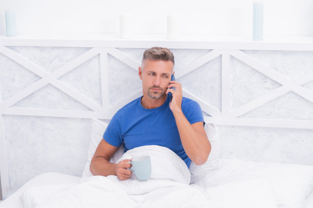 拿起话筒，大声说出来。男人在床上打电话。移动电话。手机聊天。在触摸图片下载