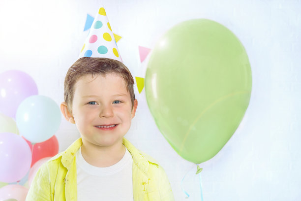 一个4-5岁的快乐孩子的肖像。气球背景上的男孩戴着节日帽。孩子望着镜框，微笑着。概念-生日，节日。图片下载