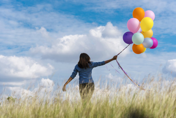 欢快可爱的女孩拿着气球在绿色的草地上奔跑，白云和蓝天洋溢着幸福。手握充满活力的气球在生日派对上玩耍快乐时光在阳光明媚的夏日户外图片下载