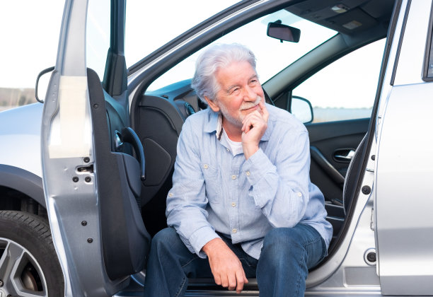 有吸引力的成年人成熟的老人，白发苍苍，坐在他停着的车微笑，看向别处图片下载