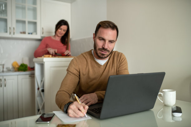 一对年轻夫妇在他们的公寓里。一个年轻人在工作，而他的妻子在厨房准备午饭。图片下载