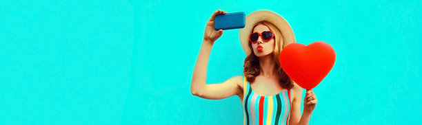 夏天的美丽的年轻女子的肖像用智能手机与红色心形气球在蓝色的背景上戴太阳镜自拍，空白的拷贝空间为你的广告图片下载