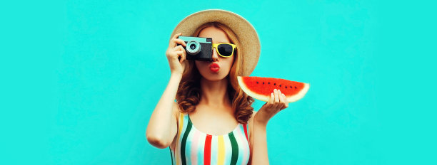 夏天的时尚年轻女子的肖像与复古电影相机和新鲜西瓜片戴着草帽摆姿势在蓝色背景图片下载