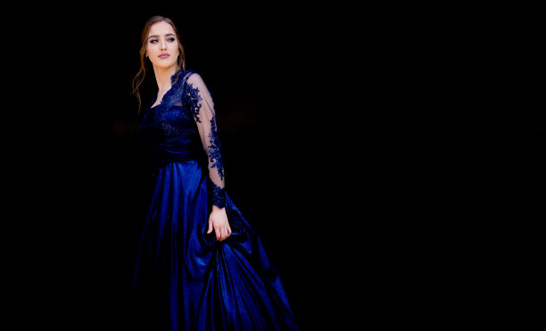 十几岁的女孩穿着美丽的深蓝色舞会礼服。黑色背景。图片下载