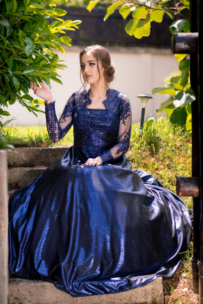 美丽的女孩坐在树下，穿着迷人的深蓝色连衣裙。图片下载