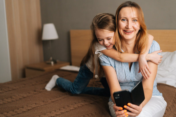 欢快的小女孩拥抱美丽的母亲的肖像，拿着手机，看着相机，视频通话聊天图片下载