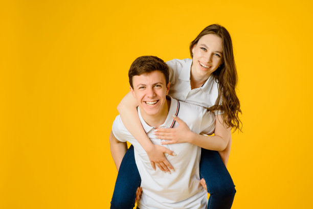 一对年轻幸福的夫妇，穿着白色t恤，在黄色的背景下微笑和大笑。图片下载