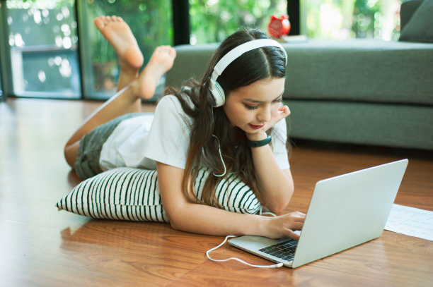 女孩躺在枕头上看电影，听音乐从笔记本电脑上的互联网。图片下载