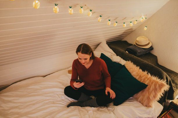 年轻女子坐在床上用智能手机图片下载