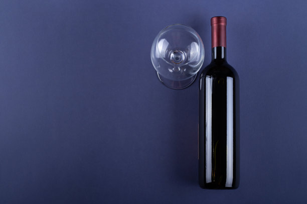 一瓶没有标签的红酒和一个紫色纸背景的空杯子。模拟饮料与地方为您的标签和文本。空间的文本。图片下载