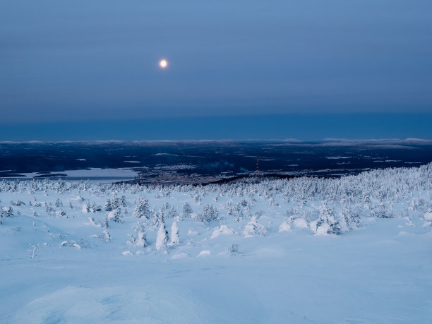 冬季，一轮满月落在冰雪覆盖的极地山坡上，遥望俄罗斯北部港口城市坎德拉克沙。冬天的极地景观。寒冷的冬天的天气。严酷的北方气候。图片下载