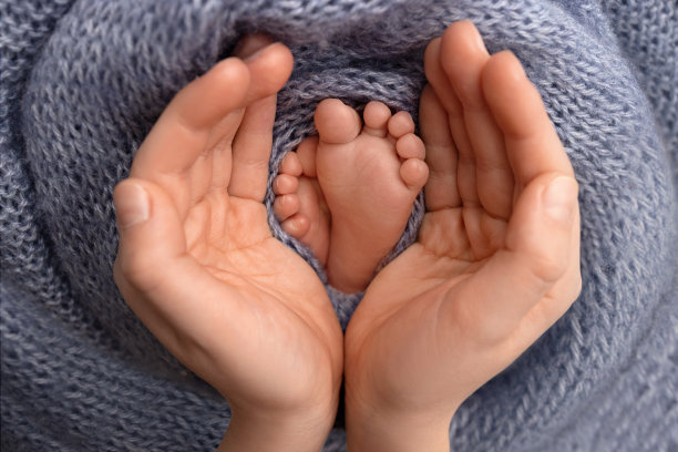 父亲的手掌，母亲的手掌，正用蓝色的毯子抱着新生婴儿的脚。新生儿的脚放在父母的手掌上。孩子的脚趾，脚跟和脚的照片。图片下载