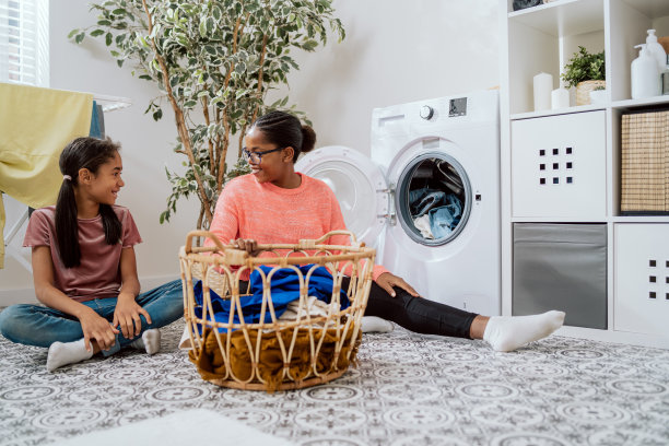 妈妈坐在洗衣房的浴室里做家务，和女儿说话，女人把脏衣服放在洗衣机里用纺纱漂洗，仔细听着孩子的微笑图片下载