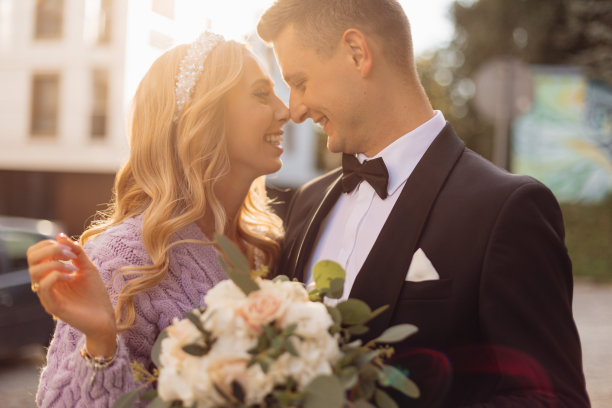 一头卷发的金发新娘笑着和穿着黑色夹克的新郎看着对方亲吻的肖像图片下载